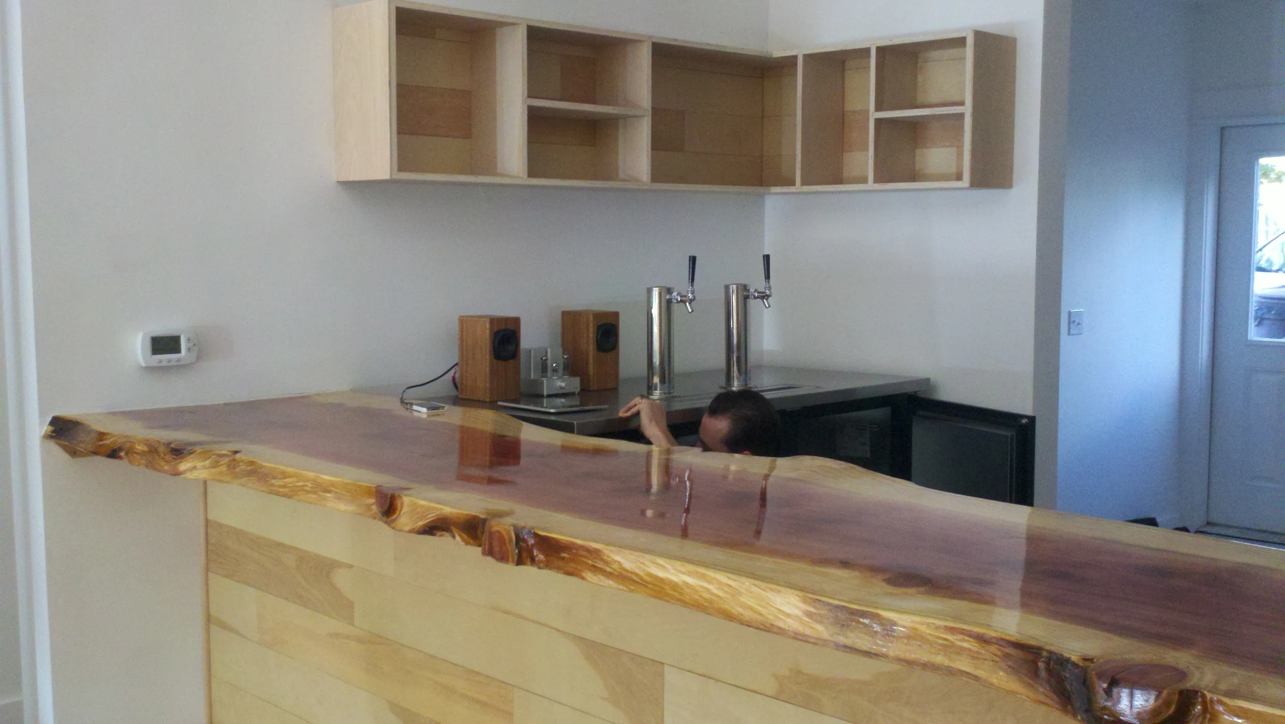 Interior of a kitchen under construction with unfinished wooden cabinets and a natural wood bar counter.