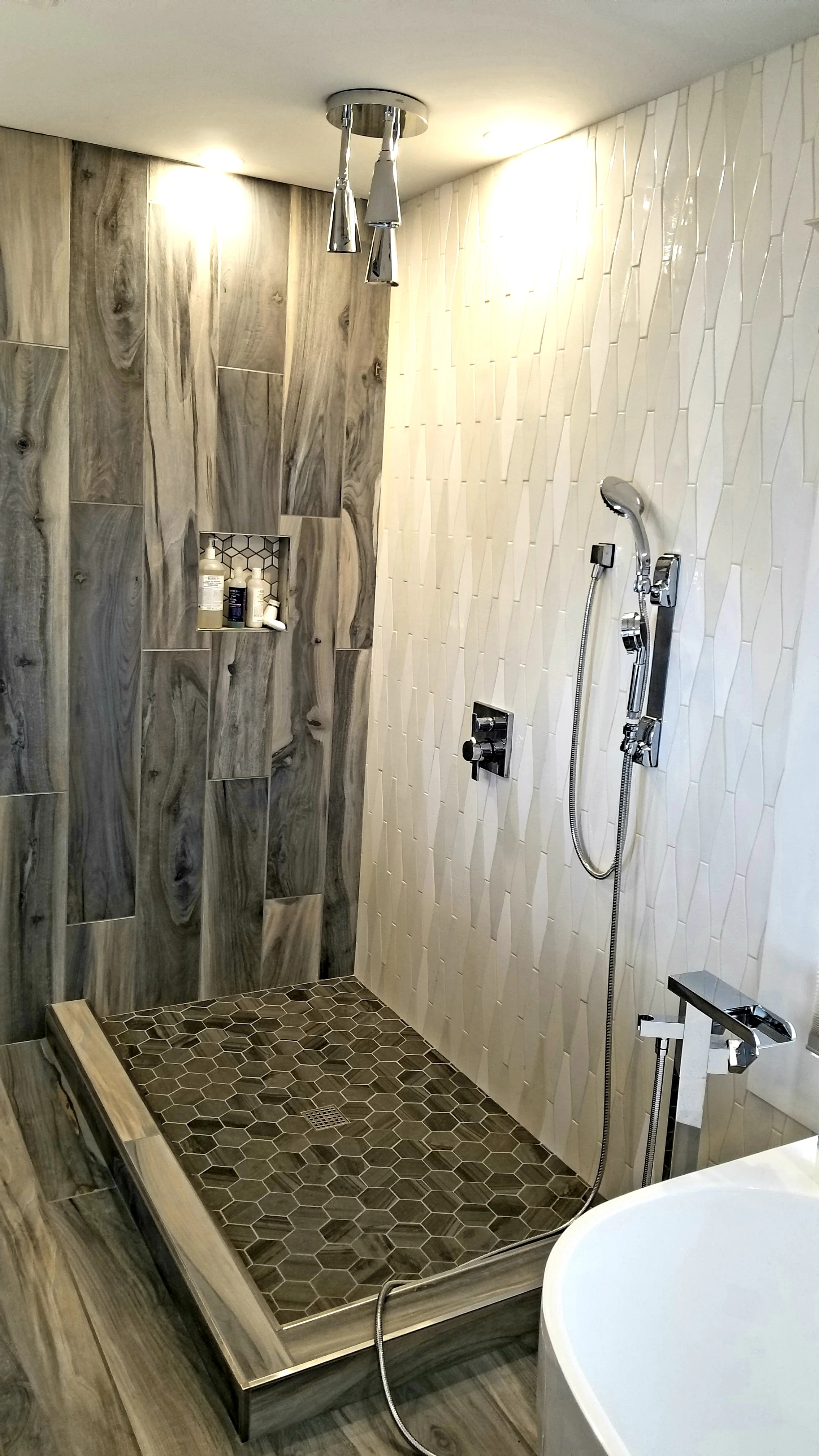 Modern shower with wood-look tiles on the wall, hexagonal dark tiles on the floor, built-in shower niche, and a handheld showerhead.