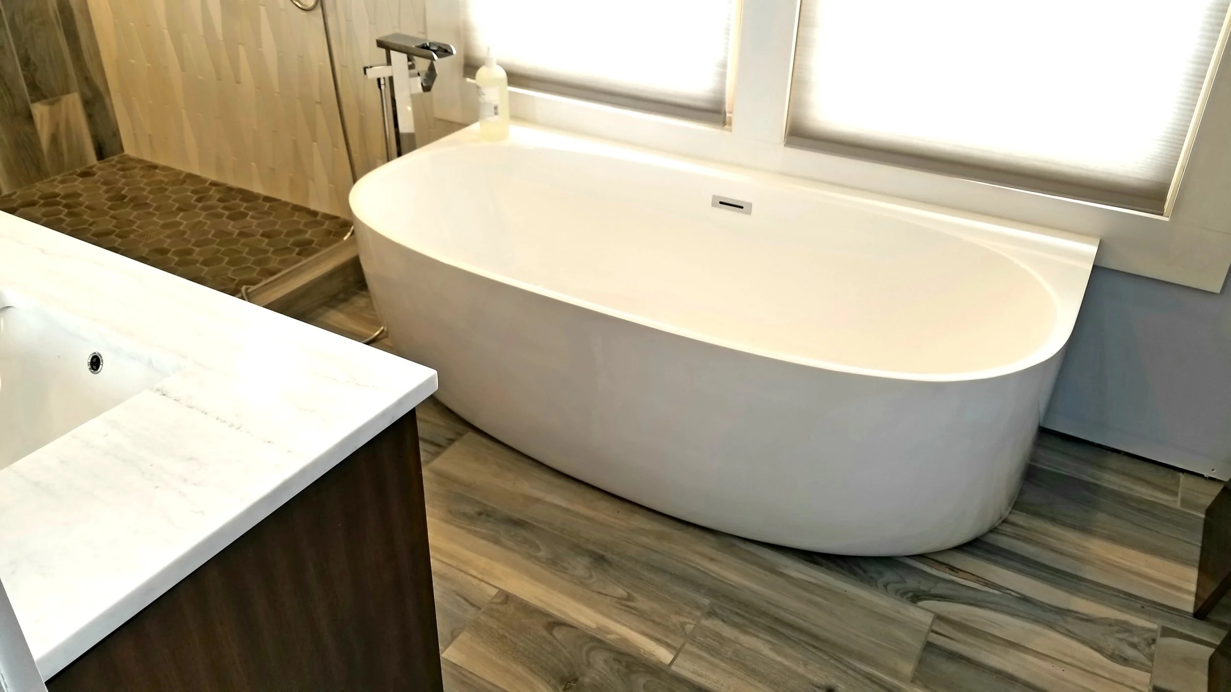 Bathroom with a large standalone bathtub, a shower area with hexagonal tile, and a white countertop with a faucet.