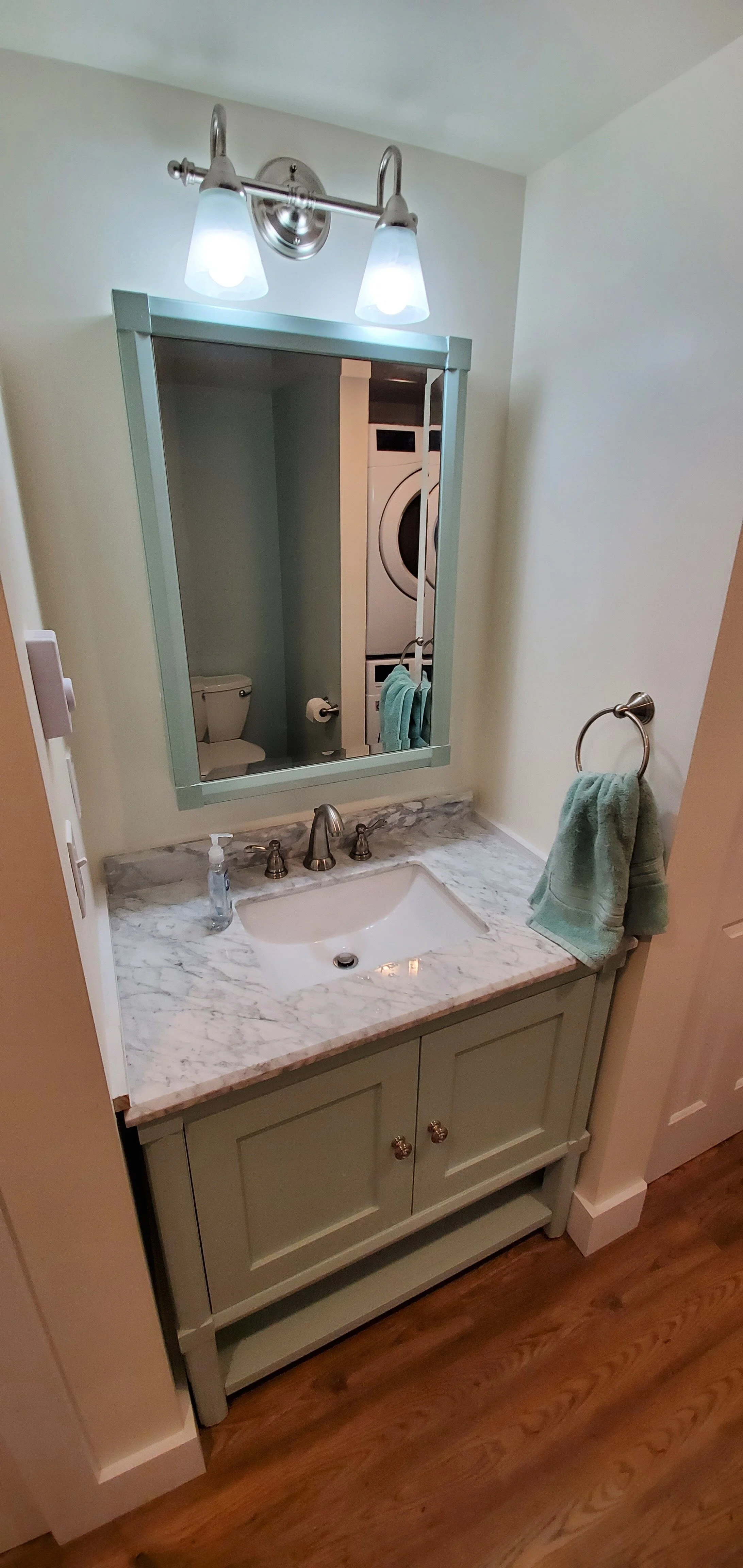Bathroom vanity with marble countertop, sink, and mirror; towel ring with a green towel and light fixture above the mirror.