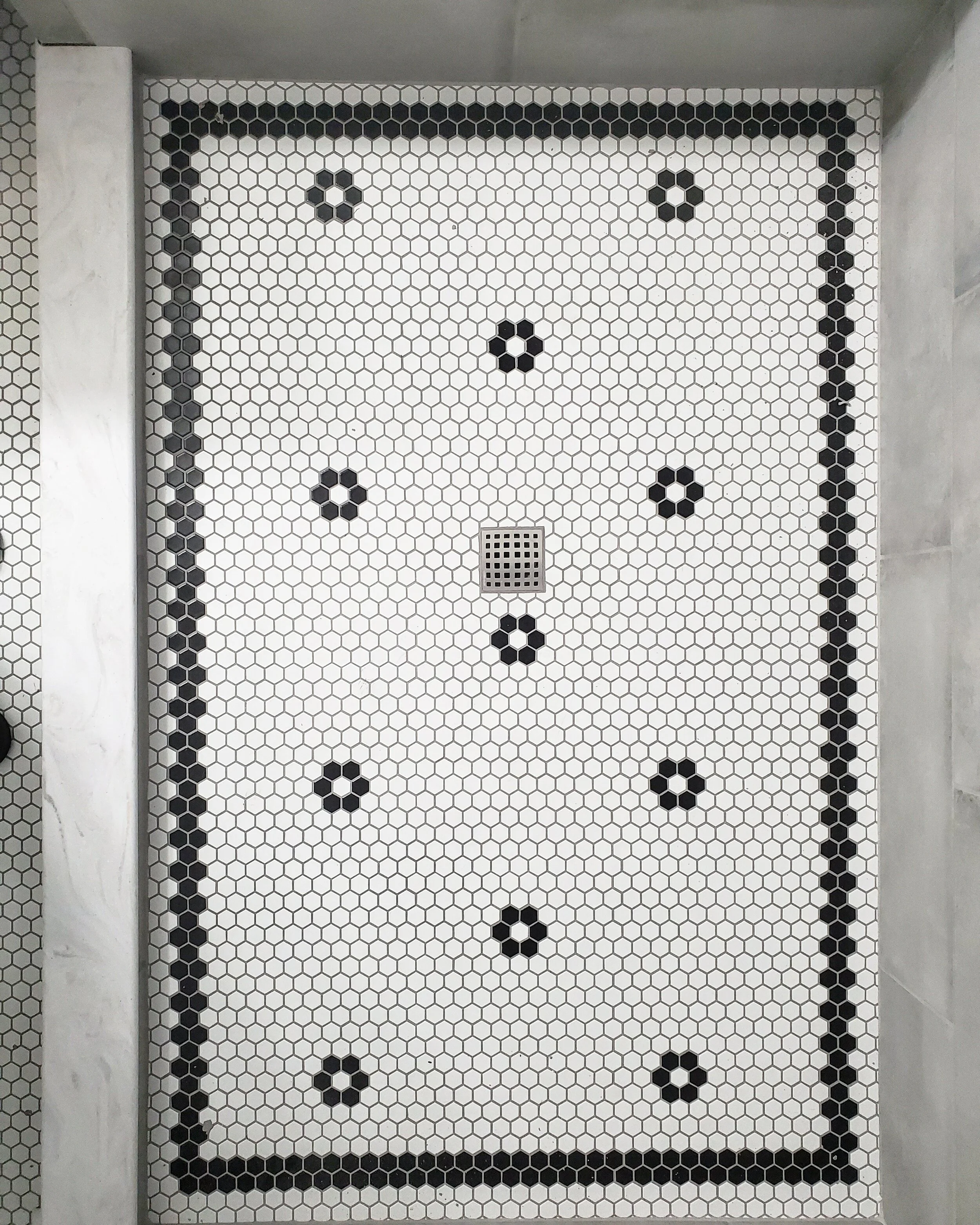 White tiled shower floor with black hexagonal accents and a drain in the center.