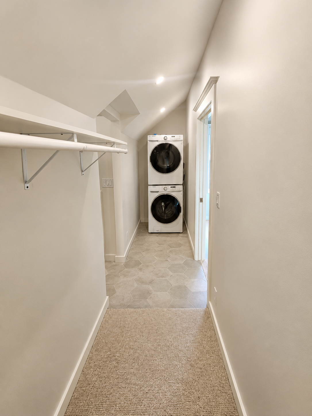 Newly framed laundry room with stacked washer and dryer, tile flooring, and built-in shelving as part of a Northeast Portland primary suite remodel.