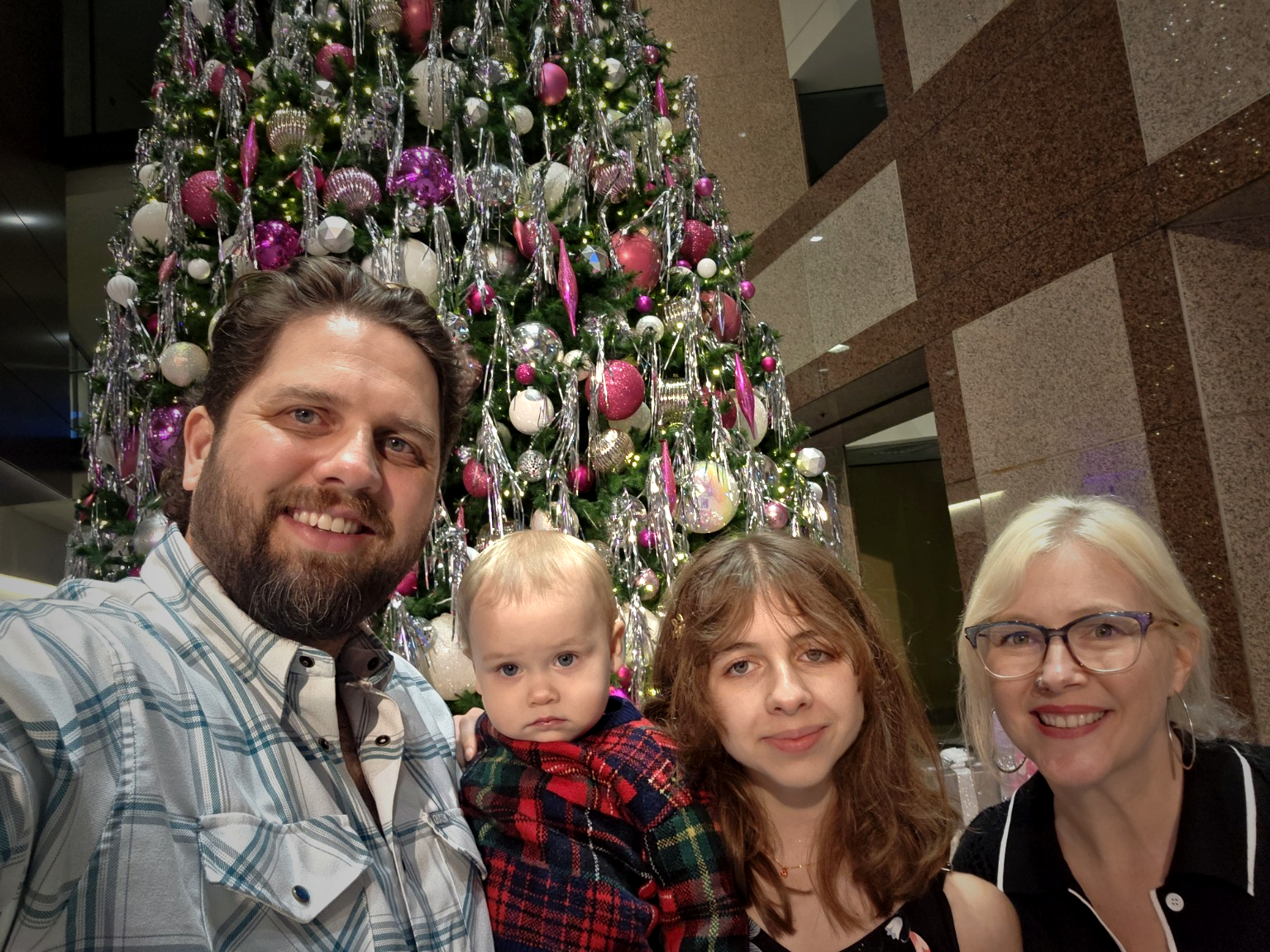 A family of four taking a selfie in front of a decorated Christmas tree